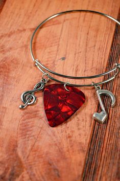 a bracelet with a red guitar pick and music note charm on it, sitting on a wooden surface