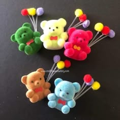 four different colored teddy bears on a black surface with colorful pom poms attached to them