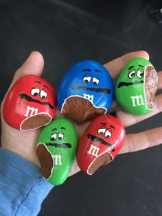 four rocks painted to look like m & m's are in the palm of someone's hand