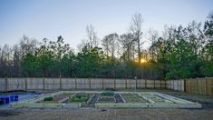 the sun is setting over an outdoor vegetable garden in front of a fenced in area