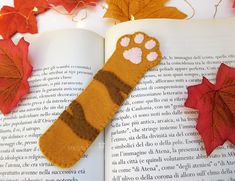 an animal paw bookmark laying on top of an open book next to autumn leaves