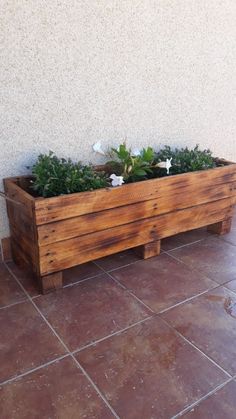 a wooden planter filled with flowers on top of a tiled floor next to a wall