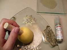 a person is holding an apple in front of a glass plate with gold decorations on it