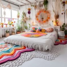 a white bed topped with lots of pillows and blankets next to potted plants on the wall