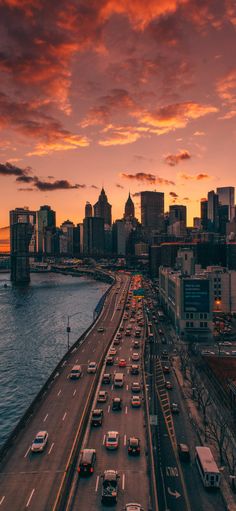 an aerial view of a city at sunset with cars driving on the road and bridge in the foreground