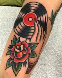 a person with a tattoo on their arm holding an old record and flower in front of them