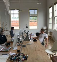 two men sitting at desks in an office with lots of clutter on the floor