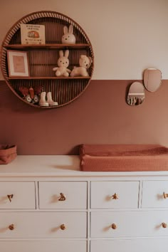 a baby's room with white dressers, pink walls and a round mirror on the wall