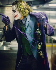 the joker is dressed in purple and holding his hands up with one hand while standing next to him