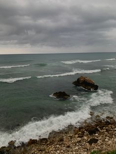 the ocean is very choppy with waves coming in to shore and rocks on the shoreline