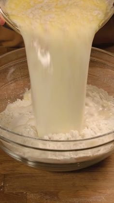 a person pouring batter into a bowl on top of a wooden table