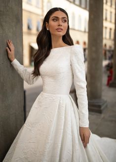 a woman in a white wedding dress leaning against a pillar with her hand on the wall