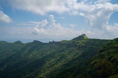 the mountains are covered with green grass and clouds in the sky, as seen from above