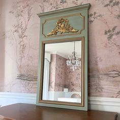 a mirror sitting on top of a wooden table in front of a wallpapered wall