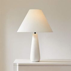 a white lamp sitting on top of a table next to a dresser with drawers in front of it