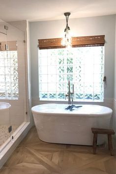 a white bath tub sitting under a window next to a wooden bench in a bathroom