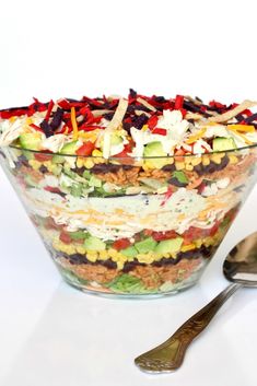 a large salad in a glass bowl next to a spoon