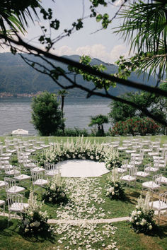 an outdoor ceremony set up with white chairs and flowers on the grass, overlooking water