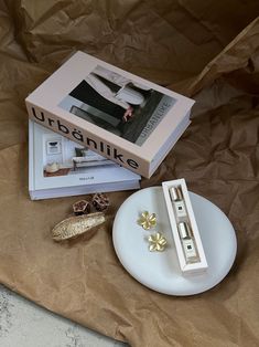 an open book and two pairs of gold earrings sitting on a plate next to a box