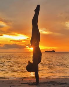 a person doing a handstand in front of the ocean at sunset or sunrise