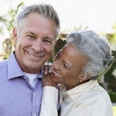 an older man and woman smiling at each other in front of a house with palm trees