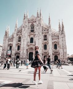 a woman in a black and white dress standing in front of a large building with tall spires