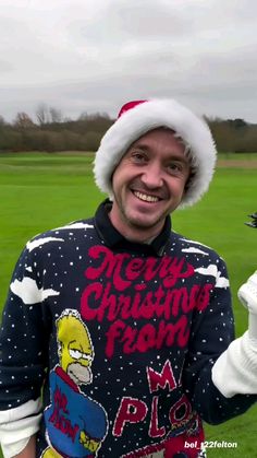 a man wearing a santa hat and holding something in one hand while standing on a field