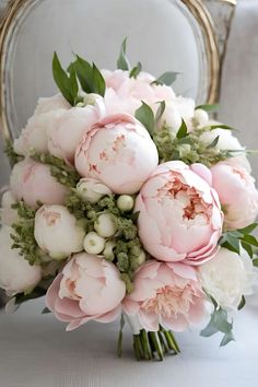 a bridal bouquet with pink peonies and greenery sits on a chair