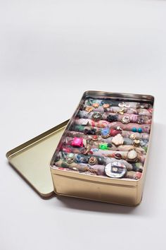 a metal container filled with lots of different types of jewelry on top of a white surface