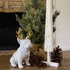 a white dog statue next to a christmas tree and pine cones on a table in front of a fireplace