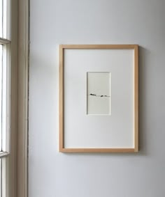 a white wall with a wooden frame hanging on it's side next to a window