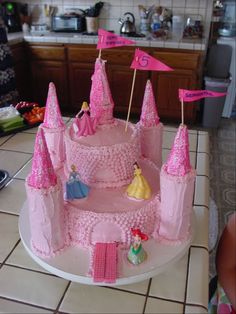 a princess castle cake with pink frosting and flags on it's top, sitting on a kitchen counter