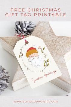 a christmas gift tag with a santa face on it and pine cones in the background