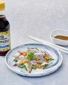 a white plate topped with salad next to a bottle of sauce and chopsticks