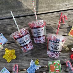 three plastic cups filled with candy canes on top of a wooden table next to other candies