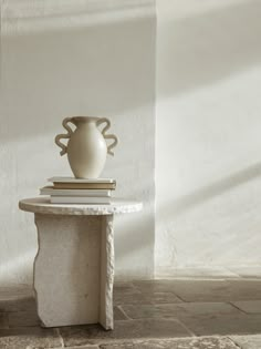 a white vase sitting on top of a table next to a stack of books in front of a wall