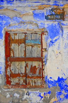 an old window with peeling paint and a street sign on the side of it,