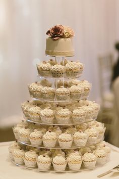 a three tiered cake with cupcakes on the bottom is displayed at a wedding reception