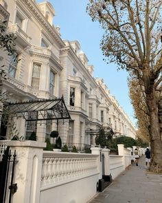 a row of white townhouses on a street with trees in the foreground and people walking down the sidewalk