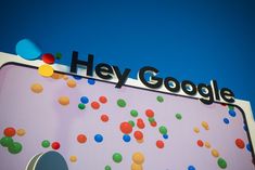 a sign that says hey google on it with colorful balls in the sky behind it