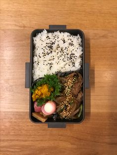 a bento box filled with rice, meat and veggies on top of a wooden table