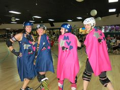 three women in roller skating gear posing for the camera on a court with people watching