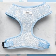 The Luxe Adjustable Neck Harness in Baby Blue Flower by Cocopup London showcases an elegant white ornate floral pattern on a baby blue background. A small white tag at the center displays the brand name, adding a touch of sophistication. This adjustable neck harness is situated on a light marble surface, making it a refined addition to your dog's accessories collection. Cute Leashes For Dogs, Cocopup London, Harness Aesthetic, Doggie Clothes, Puppy Things, Cute Dog Harness, Luxe Baby, Room Things, Dogs Stuff