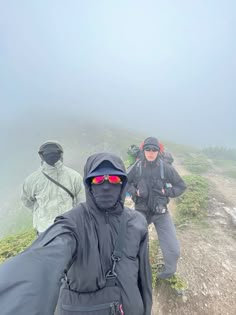 three people standing on top of a mountain with fog in the air and one person wearing goggles