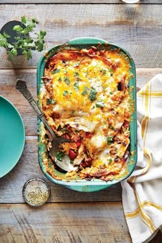 a casserole dish with meat and vegetables on a wooden table next to two plates