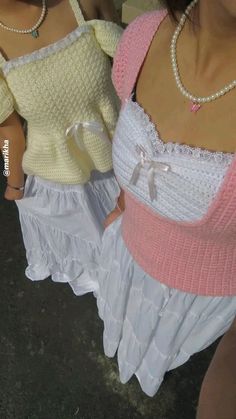 two women wearing white and pink clothing with pearls on their necklaces, one holding a cell phone