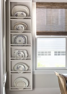 a dining room table and chairs with plates on the shelves in front of it, next to a window