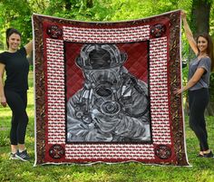 two women standing next to a large quilt with a painting of a man in a gas mask on it