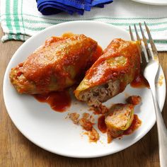 two stuffed cabbages on a white plate with fork and knife next to the plate