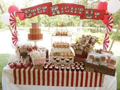 a red and white table topped with cupcakes and cake next to a sign that says step right up